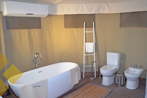 Tent bathroom with white bathtub, toilet and bidet